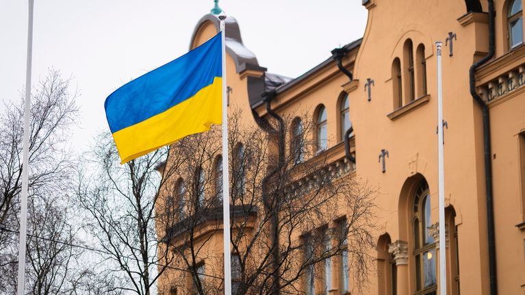 bilden visar en ukrainsk flagga som vajar framför en stor byggnad med klassisk arkitektur.
