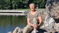 Kvinna iklädd ljusbruna kläder sitter på klipporna en sommardag. 