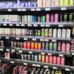 A collection of different branded energy drinks in a shop fridge. Price tags are seen on the shelves.