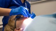 A child in a dentist's chair having his teeth examined by a dentist wearing blue gloves.