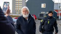 Poliisi saattaa Paul Watsonia ja toinen henkilö ottaa kuvaa tilanteesta ulkona.
