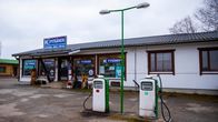 Valkoinen yksikerroksinen Pitkäsen kyläkaupan rakennus. Talon edessä vanhanaikaiset bensapumput.