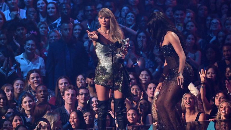 Taylor Swift seisoo lavalla palkinnon kanssa. Lavalla on myös Megan Thee Stallion ja taustalla on yleisöä.