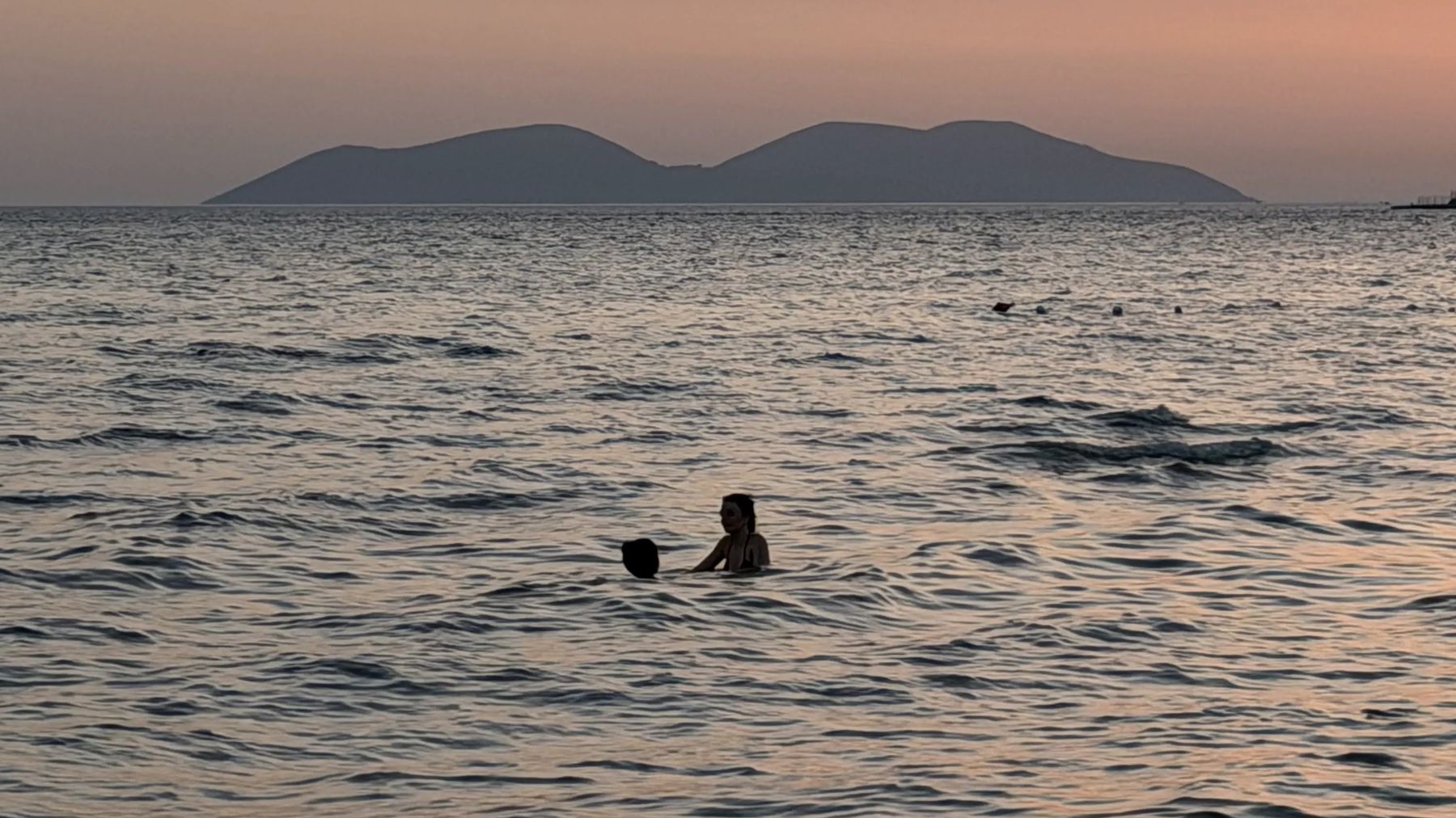 Lapset uivat auringonlaskussa ja Sazanin saari taustalla.