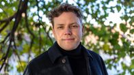 Jaakko Mustakallio katsoo suoraan kameraan. Taustalla puiden vihreitä lehtiä.