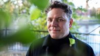 Jaakko Mustakallio katsoo suoraan kameraan. Kuvan etualalla puiden vihreitä lehtiä.