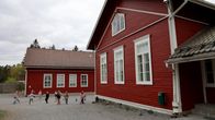 Punamultamaalattu koulurakennus, pihalla leikitään keppihevosilla.