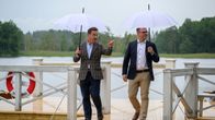 Two men holding umbrellas, walking on a dock.
