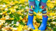 Ett barn med granna blåa stövlar och randiga strumpbyxor på en gräsmatta med gula löv.