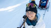 Susanna Ylinen katsoo ylös kohti kameraa ja hymyilee. Taustalla hiihtolatu ja Susannan kaksi lasta.