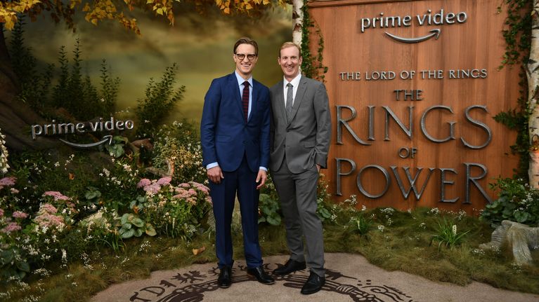 Kaksi valkoista miestä puvuissa lavasteessa, jossa lukee Prime Video ja The Rings of Power.