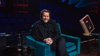Kuvassa televisio-ohjelman lavaste Elämäni Biisi, jossa Mikko Kuustonen istuu tuolilla lavalla, ympärillä tummansinisiä ja punaisia valoja.