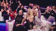 Last year's UMK winner, Erika Vikman surrounded by people sitting in easy chairs, cheering and applauding.