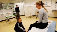 Lääketieteen opiskelijat suorittavat kliinistä tenttiä. Taustalla tentin arvioija.