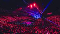 Loppuunmyyty Tampereen areena täynnä ihmisiä. Etuosassa kirkkaissa väreissä hohtava lava, joka valaisee koko yleisön purppuran sävyiseksi.