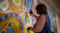 Nainen maalaamassa graffitia spraymaalilla. 