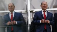 Olaf Scholz kävelee heijastavan lasin ohi, vasemmalla näkyy peilikuva