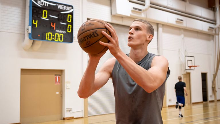 Lauri Markkanen heittää koripalloa koulun liikuntasalissa.