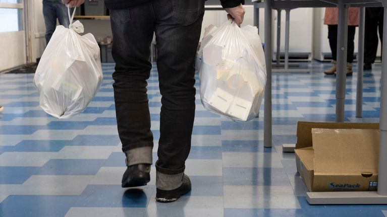 Mies kantaa kahta muovikassia Jyväskylän ruoka-avussa. Kassit ovat täynnä avustusruokaa. 