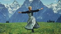 Hymyilevä nainen mekossa (näyttelijä Julie Andrews) tanssii kädet levitettyinä kukkivalla niityllä taustallaan jylhiä lumipeitteisiä vuoria.