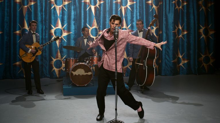 Elokuvahahmo Elvis tanssii mikrofonin edessä lavalla, taustalla yhtye.