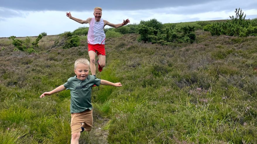 Mårten Boström och hans son Hugo springer ner för en grässluttning med utbredda armar.
