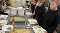 Oppilaat jonottavat ruokalassa ottamassa ruokaa linjastolta, tarjolla kastikkeita ja salaattia. Taustalla näkyy ruokailutila.