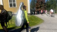 Kamarimusiikkitaiteilija kävelee sellokotelo selässään kohti Kuhmon kirkkoa.