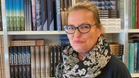 Kvinna i blå jumper framför bokhylla.