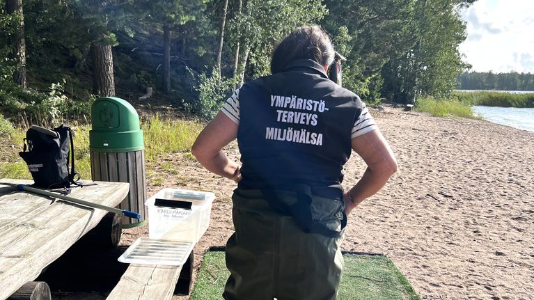 En kvinna klädd i vadarbyxor klär på sig på en strand.