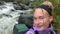 Nainen katsoo kameraan kosken edessä. 