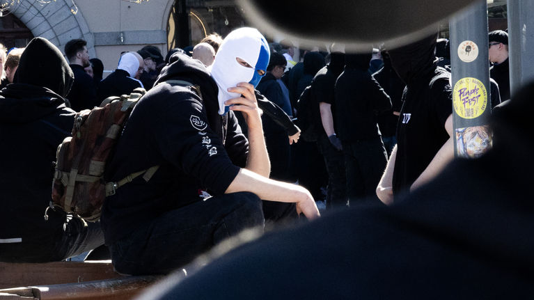 Many people dressed in black at a far-right May Day event in Tampere, one of the participants' faces is covered with a blue and white balaclava. 