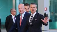Pete Hegseth ja Matthew Whitaker puvuissa kävelevät vierekkäin. Hegsethillä on käsi ojennettuna.