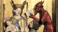 Keskiaikainen veistos kirkossa. Kuvattuna Neitsyt Maria Jeesus-lapsen kanssa, joku rukoilee polvillaan. Piru tarjoaa kirjaa (?)