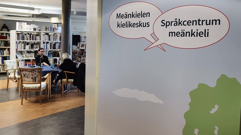 Meänkielen kielikeskuksen kyltti ja ihmisiä taustalla.