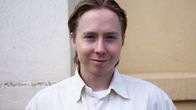 Nuorehko miesoletettu, joka katsoo kameraan ja hymyilee.