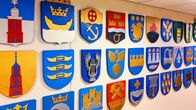 A couple of dozen municipal coats of arms on a wall. 