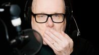 Henkilö istuu radiostudiossa käsi suun edessä.