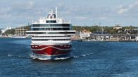 Viking Linen punavalkoinen Glory-alus poistumassa Maarianhaminan Länsisatamasta, poutainen sinitaivas, meri, taustalla Pommern-purjelaiva ja satamaterminaali.