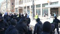 mustiin asuihin ja naamioihin pukeutuneet miehet ympäröivät polvillaan kadulla olevaa naista.