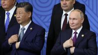 Kiinan presidentti Xi Jinping ja Venäjän presidentti Vladimir Putin seisovat yhteiskuvan eturivissä. Heillä in tummat puvut, Xillä sininen, Putinilla violetti kravatti. Presidenttien kädet ovat samassa asennossa, eli vasen käsi pitelee puvuntakin kaulusta ja oikea on takin sisällä.