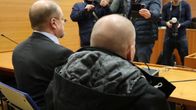 Kuvassa näkyvät henkilöt istuvat oikeussalissa. Taustalla valokuvaajat ottavat kuvia ja tekevät dokumentaatiota tilanteesta.