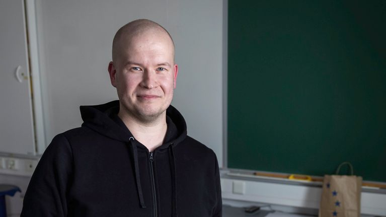 Mies nojaa pöytään luokkahuoneessa. Taustalla on liitutaulu. 