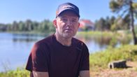 Mies istuu rannalla, taustalla siintää järvi ja koulurakennus. Veikko Feodoroff.