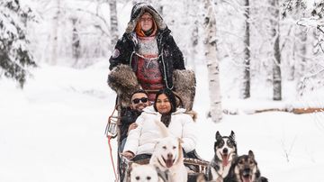 Nainen ja mies istuvat husky-reessä ja huskyt vetävät.