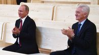 Vladimir Putin och Gennadij Timtjenko sitter bredvid varandra och applåderar.