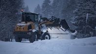 Tractor clearing snow from a road with forest in the background.