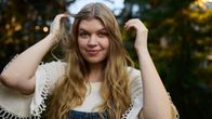 Artisti Vilma Alina nostaa hiuksiaan kädet ylhäällä ja hymyilee hieman katsoen kameraan.