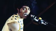 Little Richard seisoo lavalla, laulaa ja soittaa pianoa keltaisessa peilein koristellussa asussa.