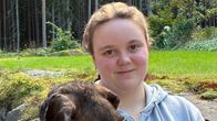 en tjugoårig flicka håller en mörk tax i sin famn.